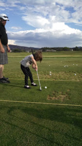 A little girl is playing golf with her dad.