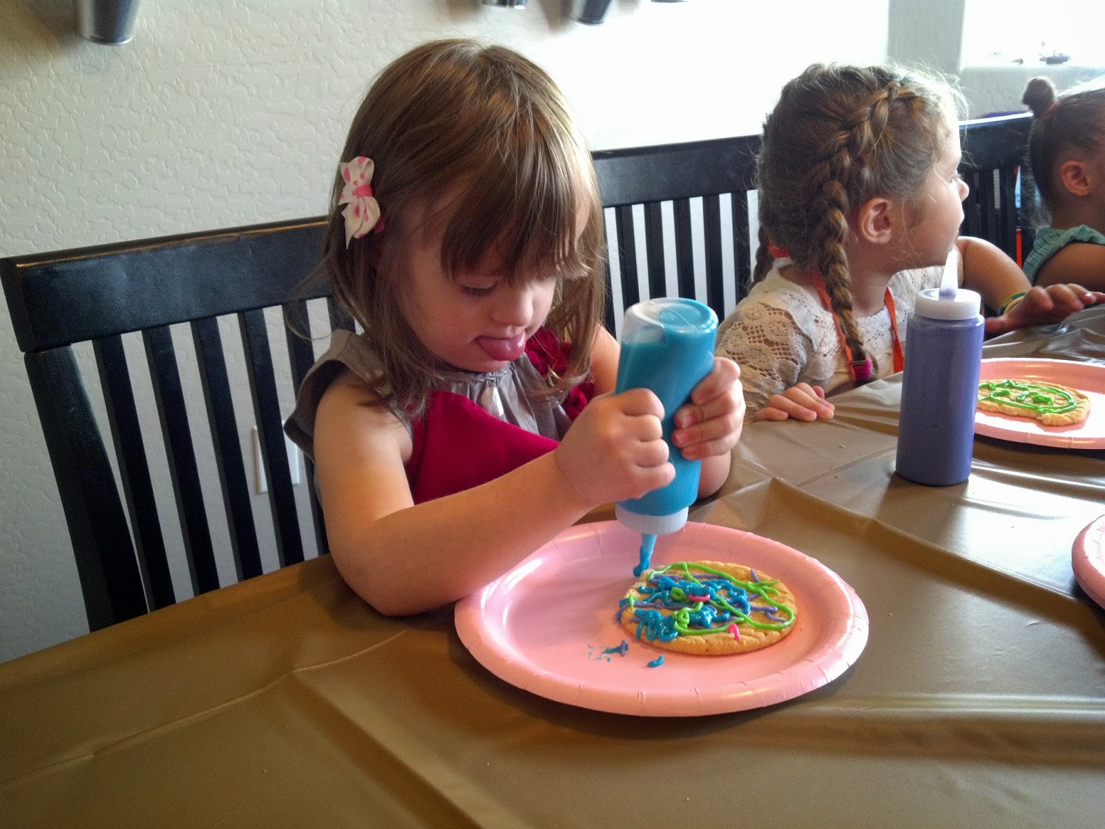 a girl with Down syndrome decorates a cookie with icing by squeezing the icing out of a condiment bottle