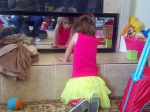 Small girl standing on her knees while looking into a mirror