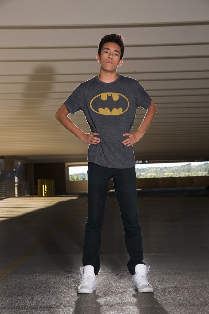 A boy wearing a batman t - shirt standing in a parking garage.