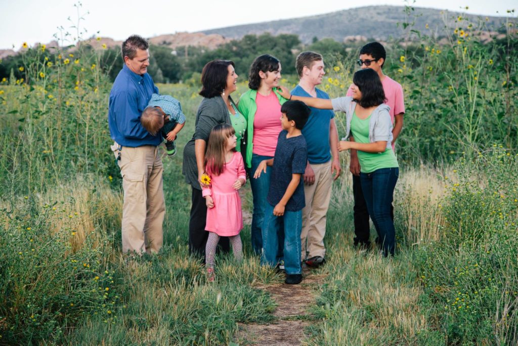 A family of 9 looking at each other while standing in a field.