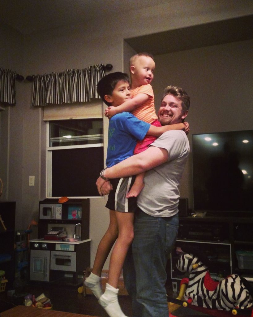 A young adult male lifts his two young brothers while the littlest clings to the middle brother. That Kid times 3