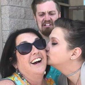 A woman is kissing a woman in front of a building.