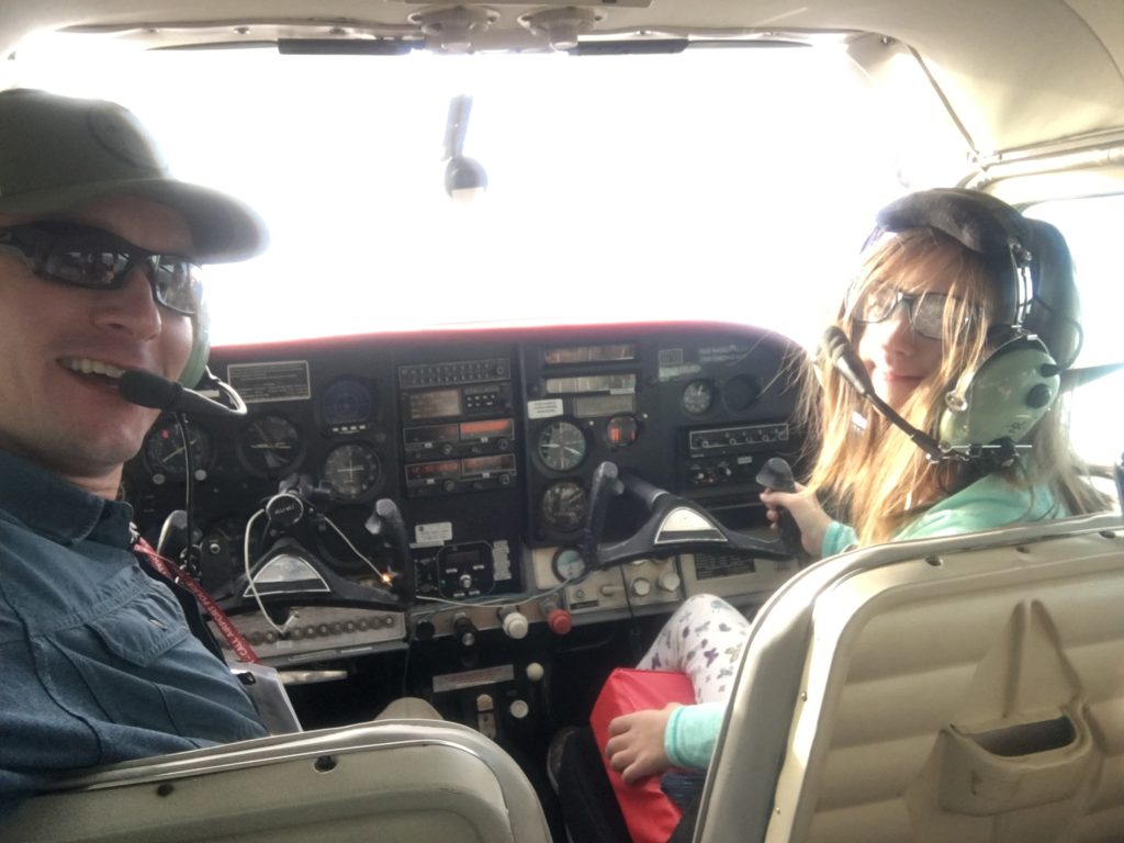 A man and a 10 year old girl who has Down syndrome sit in the cockpit of a four seat airplane.