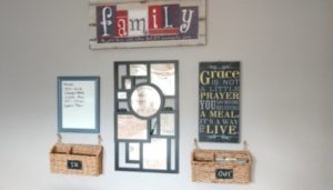 A wall with a FAQ frame with an empty frame to write on on the left and an inspiration quote on the other. Below are two baskets. The "In" basket is on the left and the "Out" basket is on the right. A canvas with a Family inspiration quote is above all.