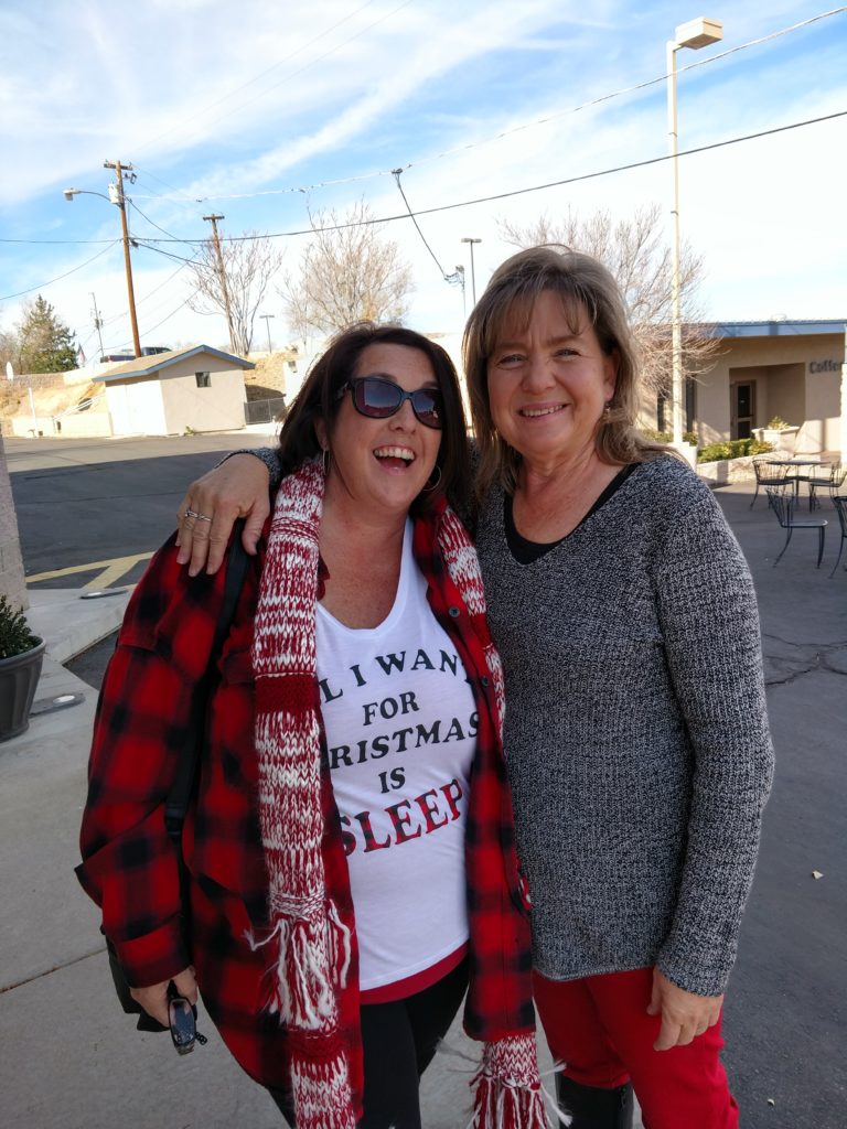 two women dressed in red, white, gray,and black standing close together each with an arm around the side of the other. One tshirt says, "All I Want for Christmas is SLEEP"