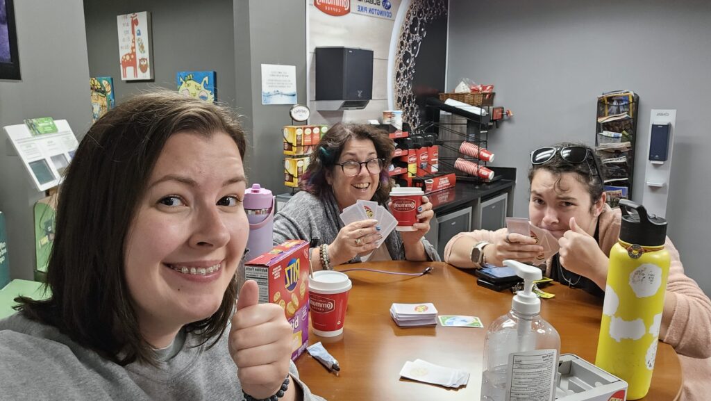 Three women playing cards and drinking coffee in the maintanence department waiting room of a car dealership