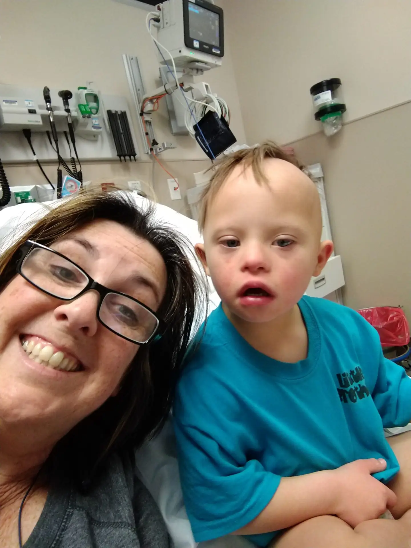 A mom with a reassuring smile, next to her son with Down syndrome who is sick in bed in the hospital