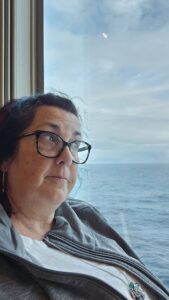 A middle aged woman leaning against her cruise cabin window pondering life while looking out to sea