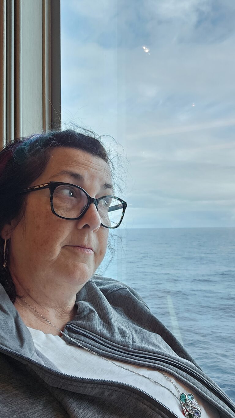 A middle aged woman leaning against her cruise cabin window pondering life while looking out to sea