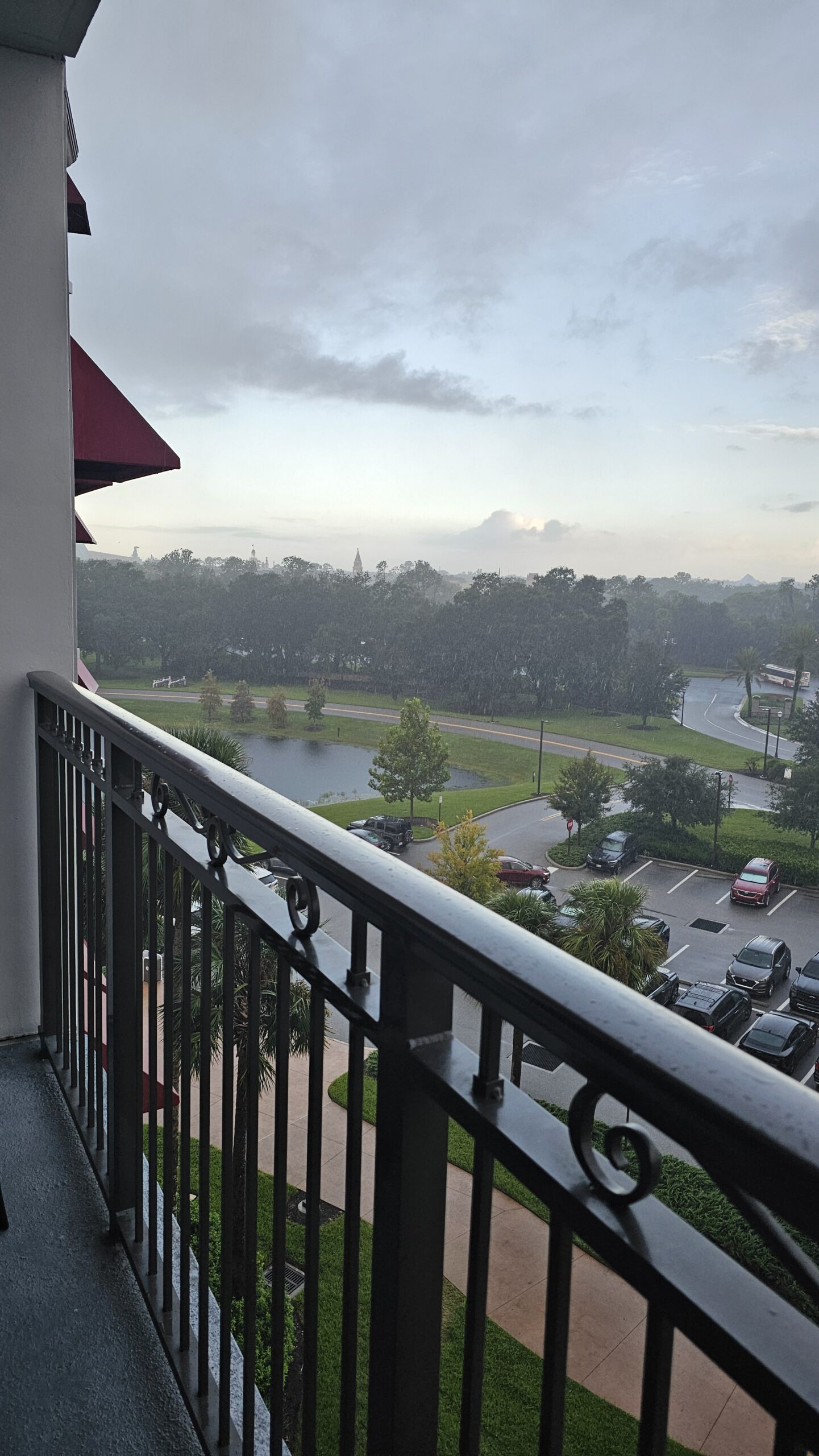 A gentle rain falls over a quiet resort landscape as seen from a covered balcony, symbolizing peace and protection in the middle of a storm.
