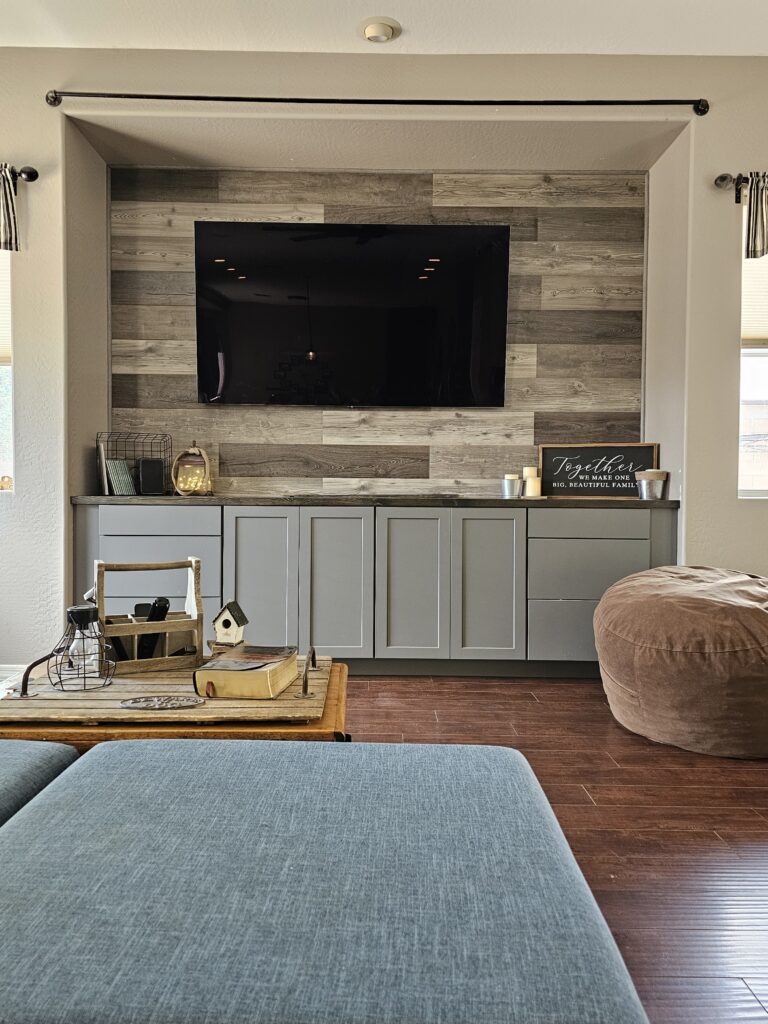 “Cozy family room with a mounted TV, gray built-in cabinets, a wood-accent wall, and a coffee table with decor.”
