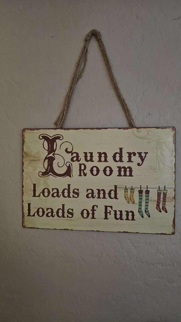 Vintage-style laundry room sign with the phrase “Laundry Room: Loads and Loads of Fun” and colorful socks hanging on a clothesline.