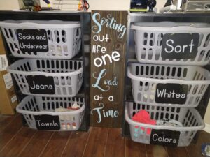 Chalkboard-labeled laundry sorter with multiple gray baskets neatly arranged on shelves for family laundry organization.