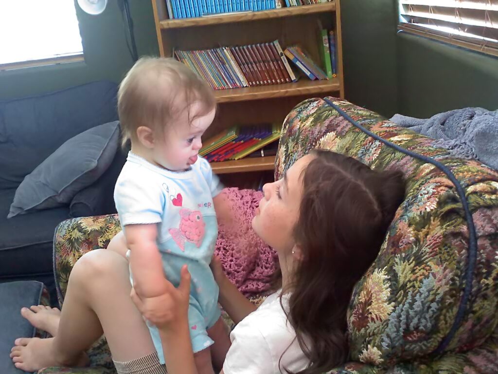 A child holding a baby while sitting together at home, showing family connection, care, and trust during a season of transition.