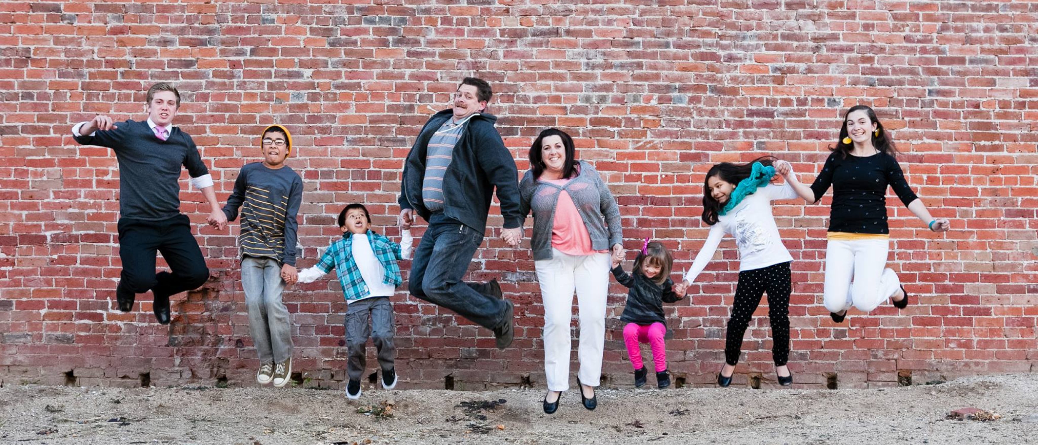 A group of people happily jumping in front of a real brick wall.