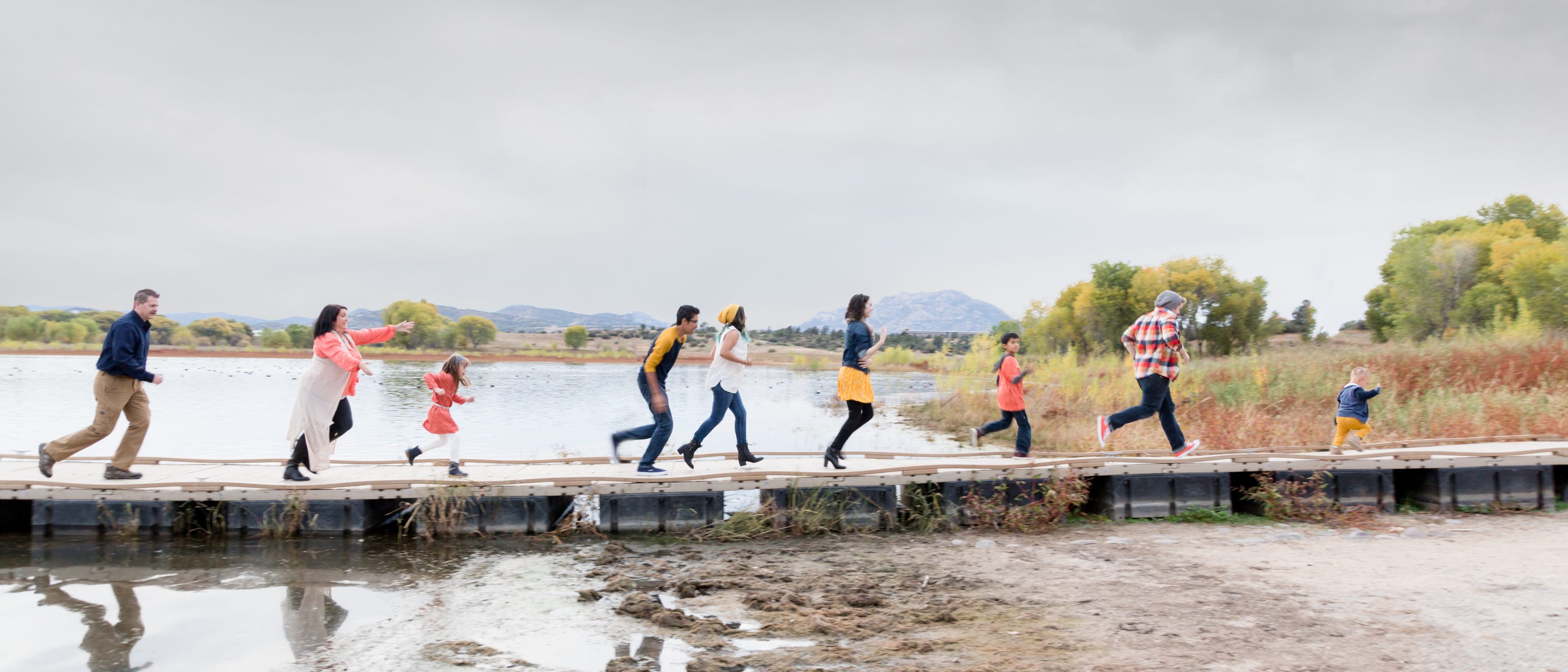 A group of people walking on a dock near a lake.